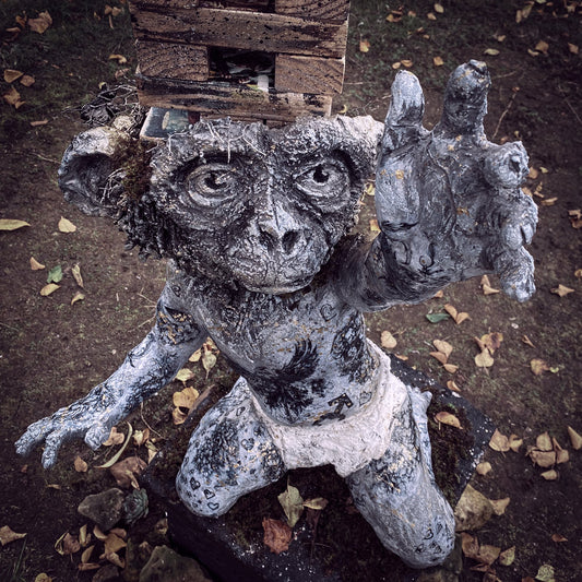 die affenbaby skulptur streckt seinenlinke hand richtung himmel und blickt hoffen gen himmel, um ihn herum herabgefallene blätter