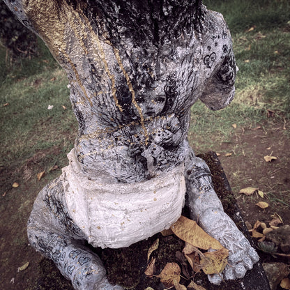 rückansicht von affenbaby statue aus beton mit einem großen engelchen bild aufseinem ganzen rücken - gold lack läuft über seine linke schulter herunter