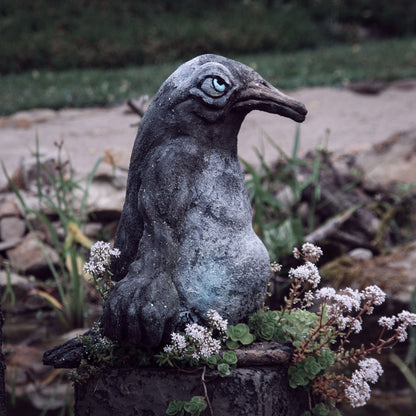 beton pinguin seitlich im profil auf sockel zwischen sedum blühend