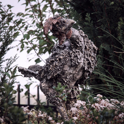 beton huhn mit wenig federn guckt neugierig zwischen hecken auf augenhöhe um die ecke
