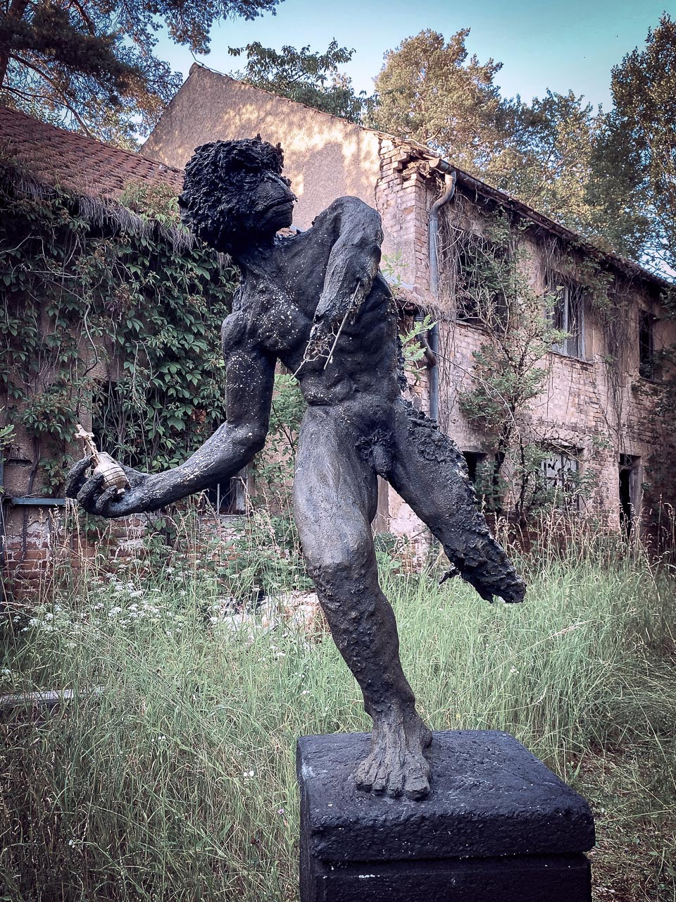 hybride menschanaffen statue auf podest hält in der hand eine goldene handgranate mit einem kreuz