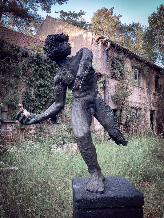 hybride menschanaffen statue auf podest hält in der hand eine goldene handgranate mit einem kreuz